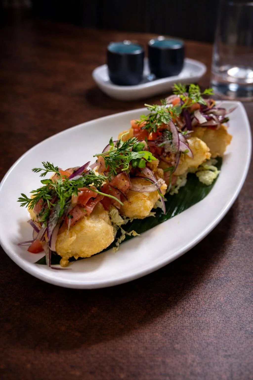 Golden fried bites topped with red onion, tomato and herbs on a white plate
