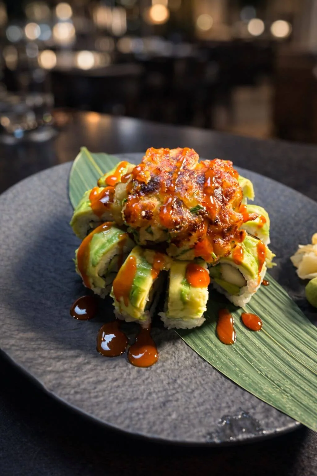 Avocado-wrapped sushi roll piled with a baked topping and orange sauce