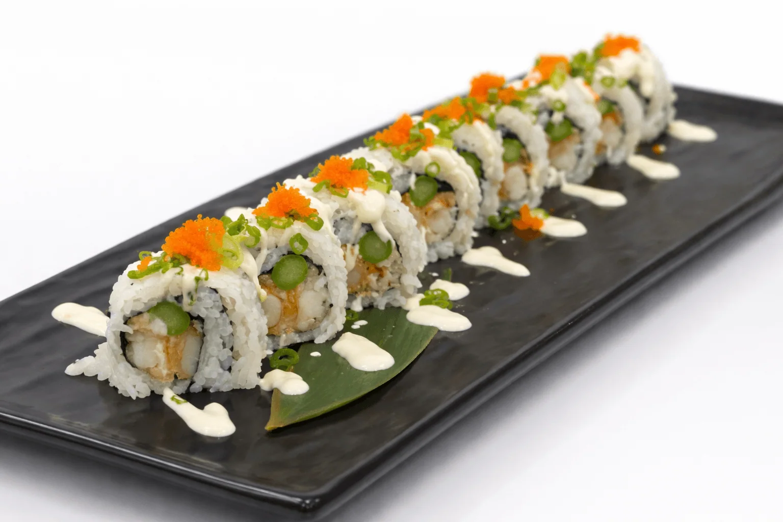 Sushi roll with asparagus, orange roe and white sauce on a black plate, white background